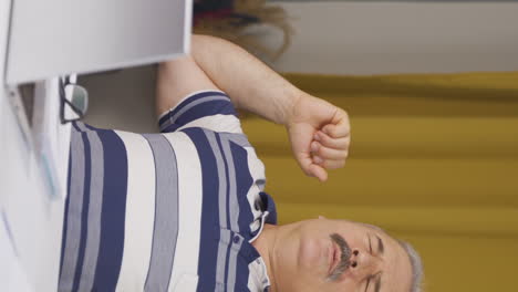 Vertical-video-of-Home-office-worker-old-man-yawns-and-relaxes-at-the-camera.